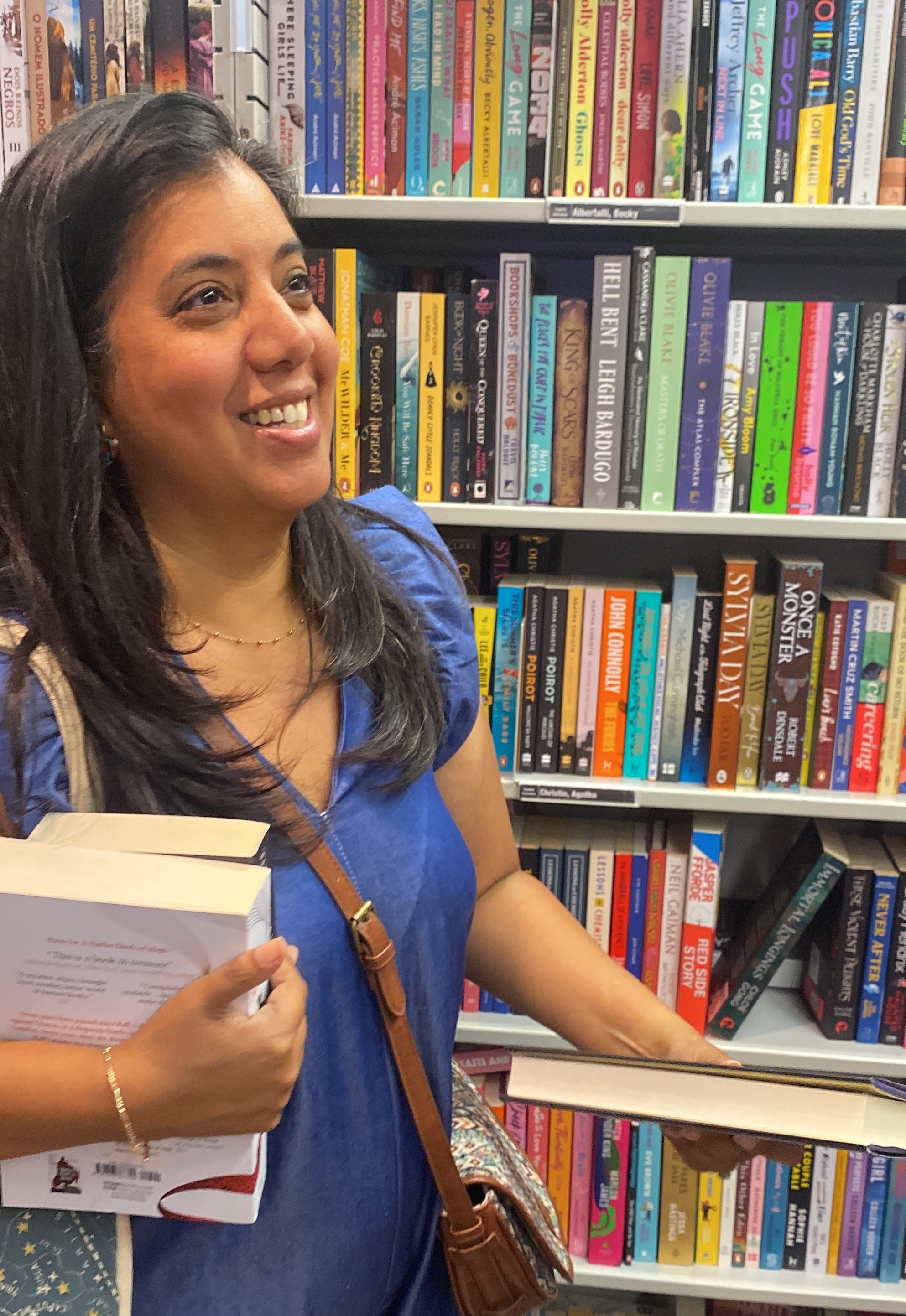 Joanna in a bookstore, holding a book and smiling in front of a wall of colorful shelves